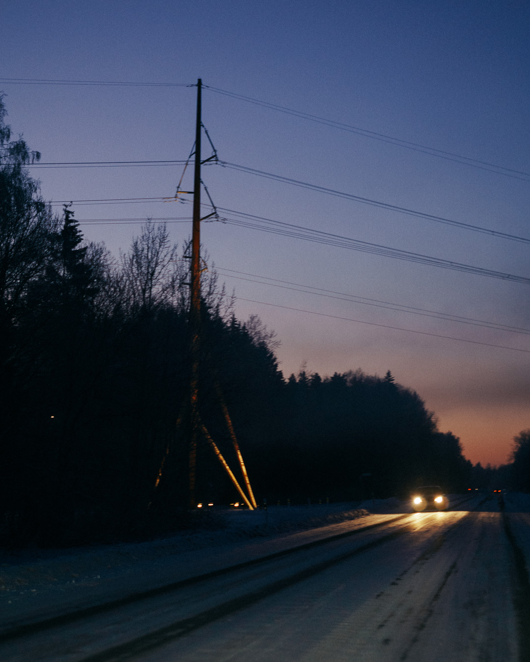 dark snowy road with electricity poles running across the sunset sky