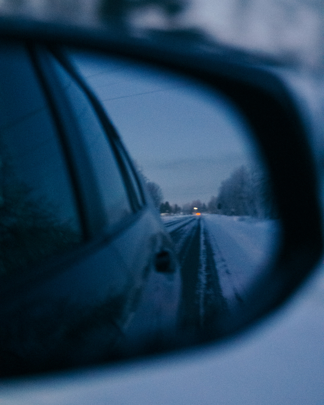 side mirror of a car showing a snowy road in the reflection