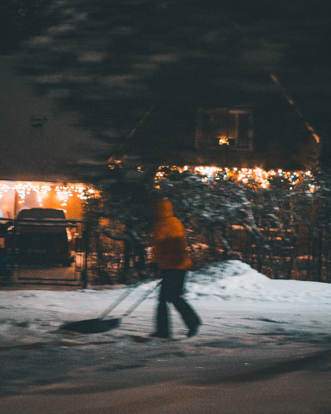 person shovelling snow in front of a house in the countryside